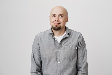 Obraz premium Portrait of funny bearded man fooling around sticking out his tongue standing over white wall. Father looks happy and enthusiastic playing with his toddler after work trying to make him laugh