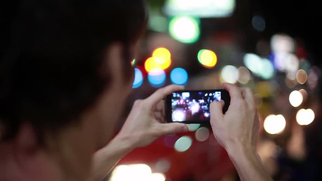 Close up of tourist with mobile phone takes picture in the night street with bokeh lights. 1920x1080