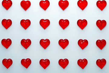 Red small shiny hearts on a white background lie in even rows.