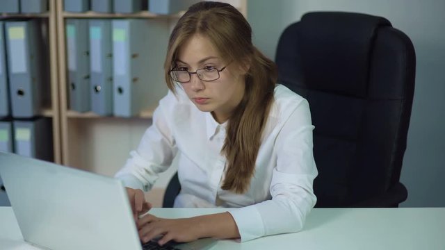 Woman in white shirt working at computer, typing and looking at screen carefully