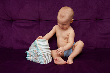 Little boy with stack of diapers or nappies on purple background