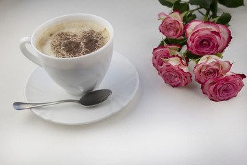 Coffee with foam with a heart of cinnamon on a white background. pink roses