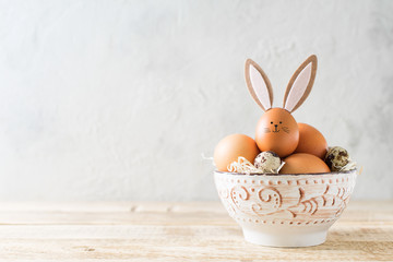 Easter bunny with eggs in bowl on grey background