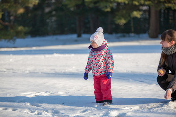 Little girl child is playing with young mother in park in the snow in winter