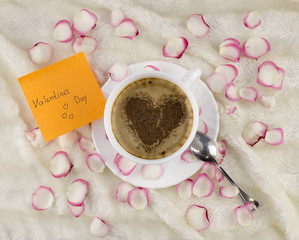 .A cup of coffee with a heart of cinnamon on a background of petals, a sticker with an inscription Valentine's Day