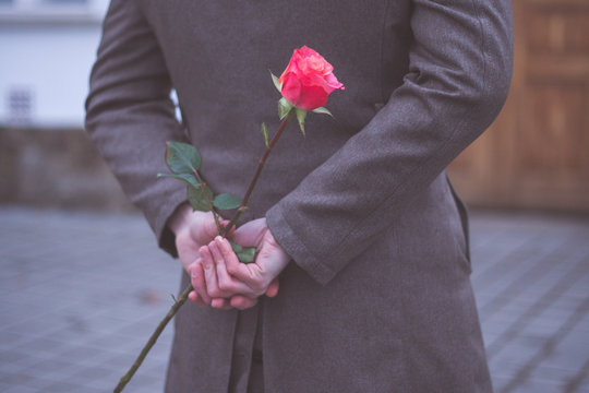 Man holding rose hiding on back at the park. Womans / Valentines Day concept.