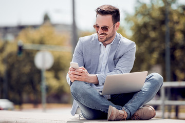 Obraz premium Young attractive man sitting outside ,using cell phone.