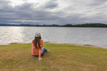 alone lady sit on lawn and look out lake view , it's relax on vacation