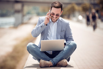 Young attractive man sitting on concrete while using cell phone.