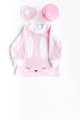 Cute pink baby clothes for girl. Shirt, toy, bottle on white background top view copy space