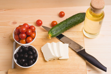 Greek salad with vegetables, feta cheese, black olives in process. Wooden background . Top view
