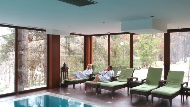 Young women relaxing together in beautiful spa laying on wooden chair near the pool
