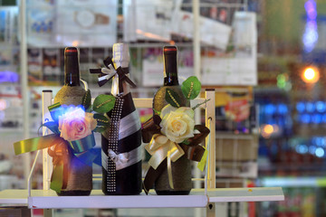 Trzy butelki wina ozdobione na prezent w sklepie na półce.