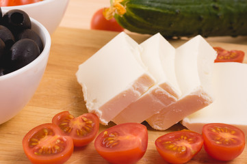 Greek salad with vegetables, feta cheese, black olives in process. Wooden background . Top view