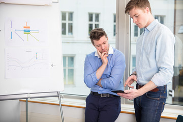 Businessmen Using Tablet Computer While Leaning On Window Sill