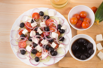Greek salad with vegetables, feta cheese, black olives in process. Wooden background . Top view