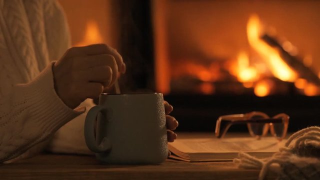 Young woman  sitting at home by the fireplace. Woman stirs mug of cocoa with spoon. 
