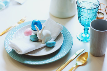 easter and spring festive table decorated in pink and blue colours with modern golden metalic cutlery, eggs and bunny.