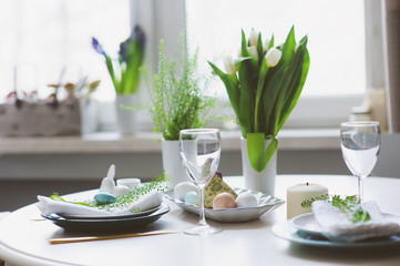 easter and spring festive table decorated in blue and white tones in natural rustic style, with eggs, bunny, fresh flowers and candles.