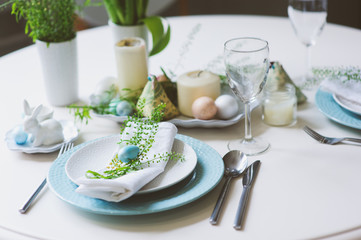 easter and spring festive table decorated in blue and white tones in natural rustic style, with eggs, bunny, fresh flowers and candles.
