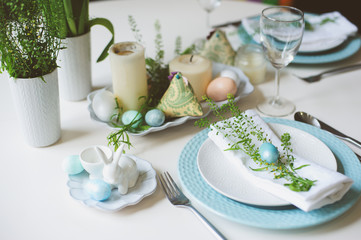 easter and spring festive table decorated in blue and white tones in natural rustic style, with eggs, bunny, fresh flowers and candles.