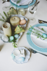 easter and spring festive table decorated in blue and white tones in natural rustic style, with eggs, bunny, fresh flowers and candles.
