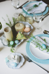 Fototapeta na wymiar easter and spring festive table decorated in blue and white tones in natural rustic style, with eggs, bunny, fresh flowers and candles.