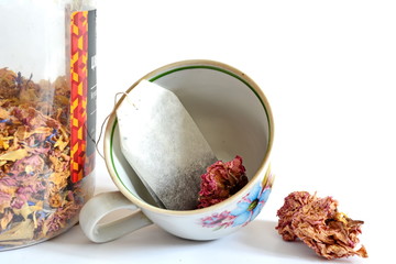 An empty pattern cup with a tea bag and part glass bank with mix of flower dry tea for brewing on a white background