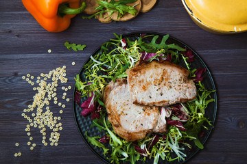 fried meat with salad, herbs, pepper on a dark wooden background. Background for the postcard.