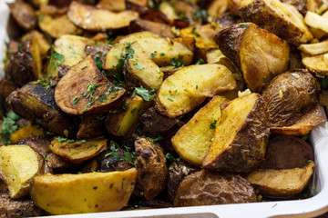 Freshly fried potato wedges with herbs and garlic on a baking sheet