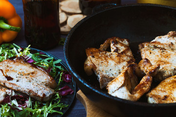 fried meat in a frying pan with salad, herbs, pepper on a dark wooden background. Background for the postcard.