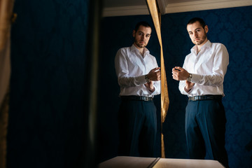 A handsome man in a white shirt buttoned his cuffs. Its reflection on the TV screen