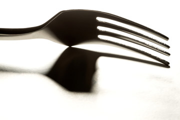 Close up of metal fork backlit with shadow on white