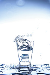 Ice dropping and water splashing in the glass with reflection on the mirror table and isolated on white background.