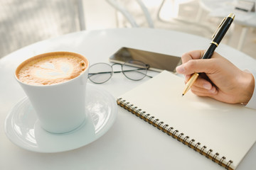 business background hand of businessman write notebook paper with coffee, glasses, mobile phone, copy space. image for technology, beverage, idea, equipment, cafe, education, workplace concept
