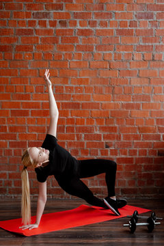 Portrait of beautiful blonde  woman in black sportswear standing against the background of a red brick wall after fitness workout.Fites concept. The girl does warm-up before a fitness training.