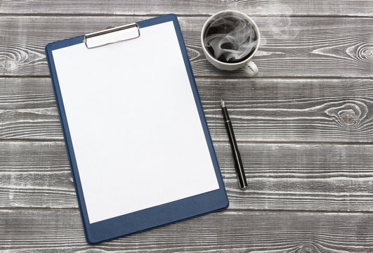 a blank sheet of paper on a tablet, a cup of coffee, a pen on the background of a wooden table.