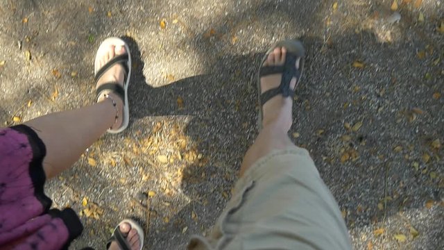 Downward POV shot of a man and woman walking, wearing sandals