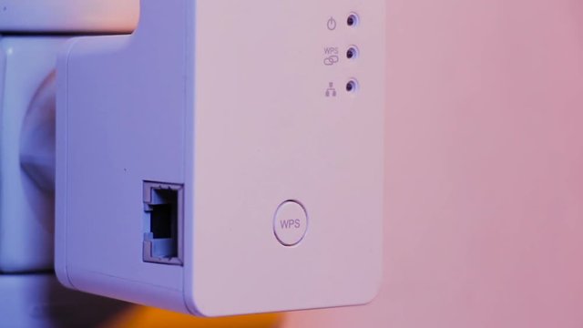 Man press with his finger on WPS button on WiFi repeater which is in electrical socket on the wall