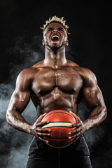 Fototapeta na wymiar Portrait of afro-american sportsman, basketball player with a ball over black background. Fit young man in sportswear holding ball.