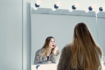 Fototapeta premium Young sexy model stands at the table in barbershop in a fluffy fur jacket. Girl looks into her reflection. Concept of opening a barbershop and attracting attention