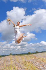A beautiful young woman dressed in white vintage clothing expresses her musical excitement with a tambourine in her hand. She leaps in the air with a blue sky  behind her.