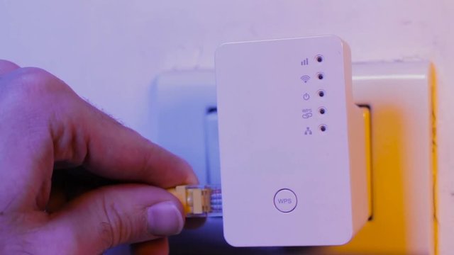 Man insert ethernet cable into WiFi extender device which is in electrical socket on the wall