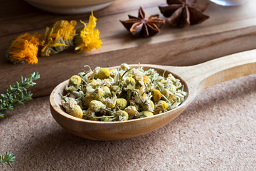 Dried chamomile on a wooden spoon, with other herbs in the background