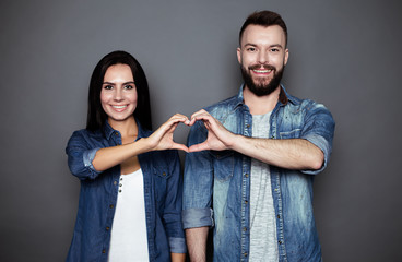 A beautiful smiling young couple in casual clothes smiling and holding hands in the shape of a...