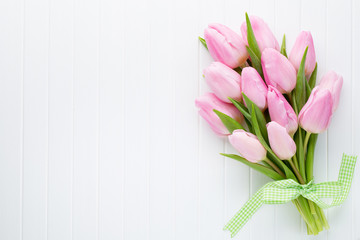 Fresh pink tulip flowers bouquet on shelf in front of wooden wall.