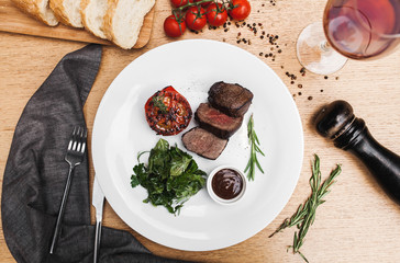steak and grilled tomatoes with greens, souce with a bread board on a wooden table