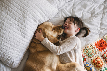 Happy Girl lying on a bed laughing and cuddling her golden retriever dog
