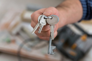 Man's hand holding keys with a construction in background