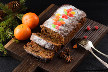 Delicious homemade fruit cake decorated with sugar icing and candied fruits served with clementines and fir branch on oak board